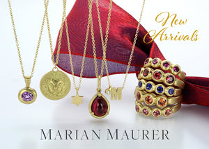 A row of 5 18k yellow gold necklaces with pendants from jewelry designer Marian Maurer with a stack of bezel set, multicolored sapphire bands