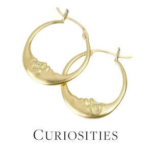 A pair of 18k yellow gold hoop earrings with carved moon faces with white diamond eyes, handcrafted by jewelry designer Anthony Lent. Link to the "curiosities" collection