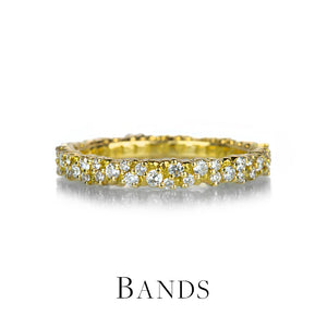 An 18k yellow gold wedding band by jewelry designer Paul Morelli covered with scattered white diamonds of various sizes across the surface. Ring sits on a white background with a faded drop shadow above text which reads, "Bands," and image links to all rings that fall into the "band" category available on the website.
