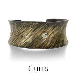 A wide oxidized iron cuff with 22k yellow gold lines on top and a round, bezel set diamond, handcrafted by jewelry designer Pat Flynn. Link to the cuff bracelet collection