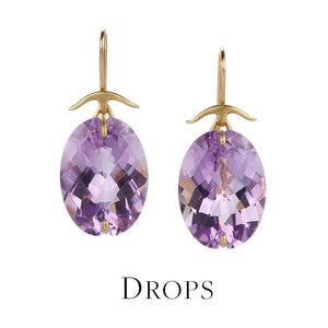 A pair of oval, faceted purple amethyst drop earrings set in 18k yellow prongs with a curved bar ear wire, handcrafted by jewelry designer Gabriella Kiss. Link to drop earrings collection