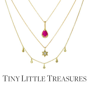 Three delicate 18k yellow gold necklaces by jewelry designer Marian Maurer. From top to bottom; a bezel set, teardrop shaped bright pink ruby pendant on a delicate chain, a small star of david pendant with a diamond in the center on a delicate gold chain, a delicate gold chain necklace with five tiny, bezel set white diamond pendants. Link to the "tiny little treasures" collection