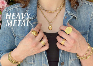 A model wearing a jean jacket and two heavy chain necklaces, a stack of gold chain bracelets and 4 heavy gold rings, all jewelry handcrafted by designers Page Sargisson, Petra Class, Ananda Khalsa, Kate Maller