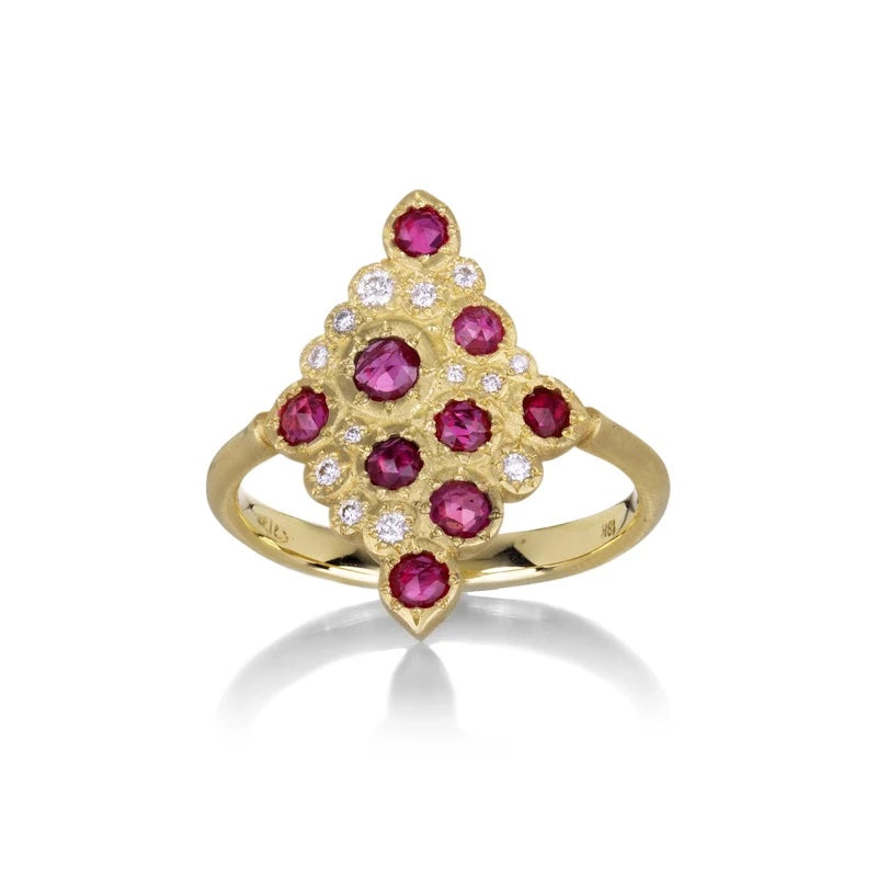 A gold ring featuring a cluster of round pinkish-red gemstones and small clear stones, photographed on a white background with a soft reflection.