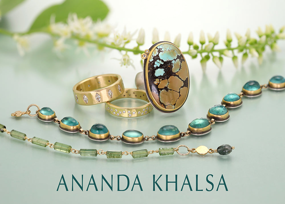 Jewelry set with rings and a necklace on a light green background, featuring the brand 'Ananda Khalsa'.