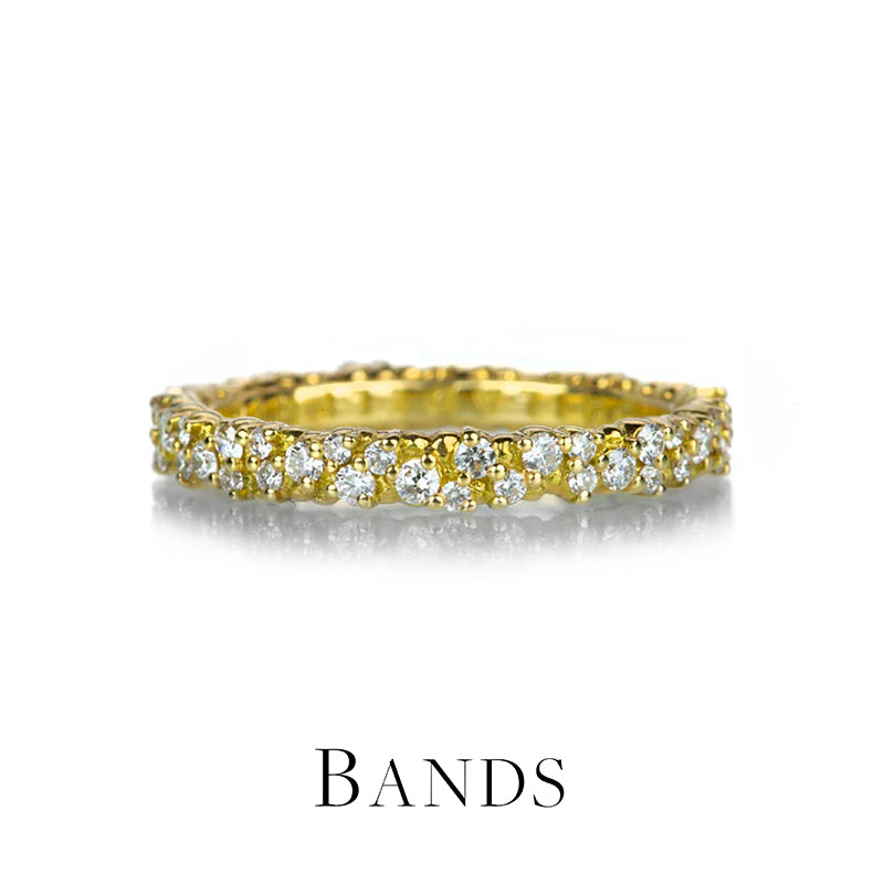 An 18k yellow gold wedding band by jewelry designer Paul Morelli covered with scattered white diamonds of various sizes across the surface. Ring sits on a white background with a faded drop shadow above text which reads, "Bands," and image links to all rings that fall into the "band" category available on the website.
