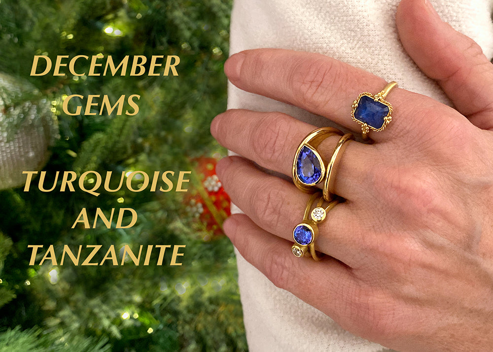 Hand wearing gold rings with blue gemstones against a blurred green background