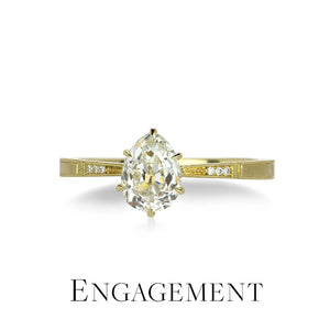 Gold engagement ring with a pear-shaped diamond on a white background