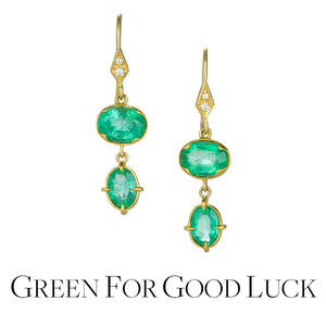 A pair of 18k yellow gold earrings with a horizontally set, faceted, oval emerald drop set in a scalloped bezel, paired with a vertically set faceted oval emerald drop, handcrafted by jewelry designer Annie Fensterstock