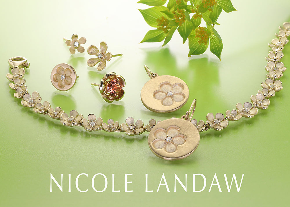 Nicole Landaw gold jewelry set featuring a floral chain necklace, matching earrings, and a flower-shaped pendant, displayed on a light green background with a leaf prop.